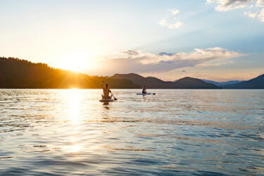 two people paddleboarding on a lake at sunset