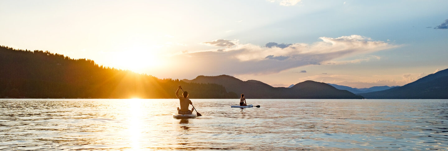two people paddleboarding on a lake during sunset