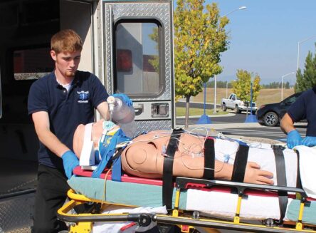 paramedicine students transfer a medical manniquin from the back of an ambulance to a wheeled patient gurney