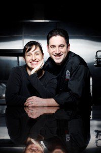 a man and a woman wearing chef uniforms pose in a kitchen