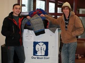two students pose next to coat donation box