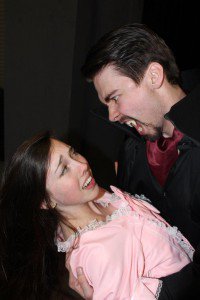 two theatre students acting in a production of dracula, a man dressed as a vampire bares fangs at a woman
