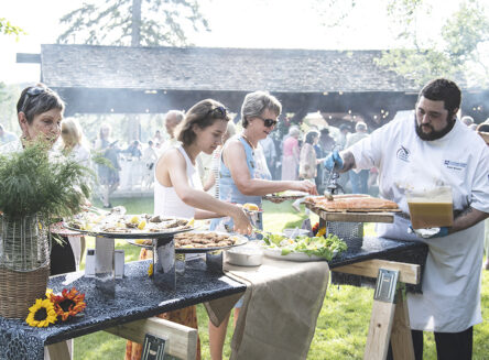 a chef and guests around a serving table