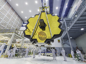 james webb space telescope being hoisted by a crane surrounded by technicians