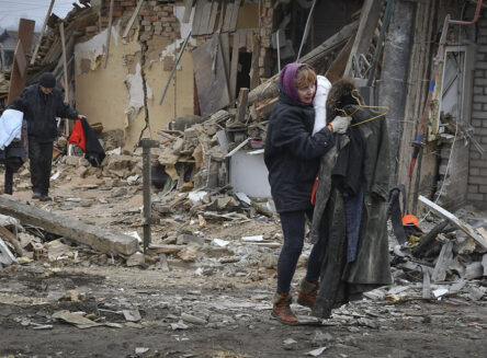 a ukrainian woman and man carry their belongings walking amongst the bombed out remains of their homes