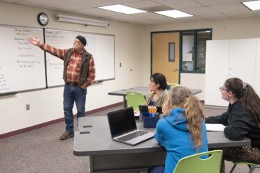a teacher pointing at a whiteboard in a classroom while students listen
