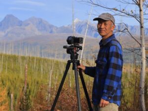 wildlife photographer sumio harada stands next to his camera and with a mountain range in the background