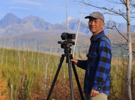wildlife photographer sumio harada stands next to his camera and with a mountain range in the background