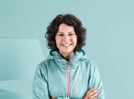 Austrian mountaineer Gerlinde Kaltenbrunner headshot. She is wearing a turquoise jacket with a plain turquoise background