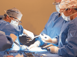 Four FVCC surgical technology students are operating on a dummy, guided by an instructor. They are dressed in scrubs, surgical caps, masks, and gloves, and are focused on the task with surgical tools in hand.