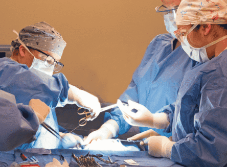 Four FVCC surgical technology students are operating on a dummy, guided by an instructor. They are dressed in scrubs, surgical caps, masks, and gloves, and are focused on the task with surgical tools in hand.
