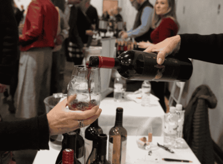 A promotional graphic for the 18th Annual Grand Wine Tasting, featuring photos of culinary delights, wine being poured, and guests celebrating.