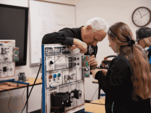 An instructor and a student work together on an Electrical Controls Training System board in a classroom.