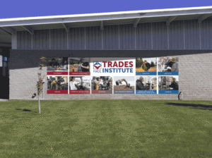 he exterior of the FVCC Trades Institute building, formerly known as the Occupational Trades building, featuring a large white sign with red and blue lettering and a collage of photos showing various trade programs.