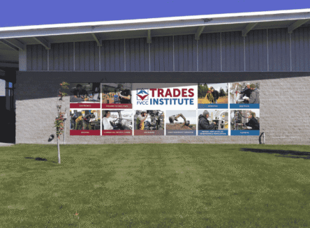 he exterior of the FVCC Trades Institute building, formerly known as the Occupational Trades building, featuring a large white sign with red and blue lettering and a collage of photos showing various trade programs.