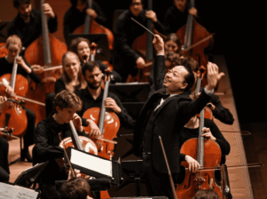 Chung Park leading the St. Olaf Orchestra on stage at Orchestra Hall, with cellists and bassists performing in the background.