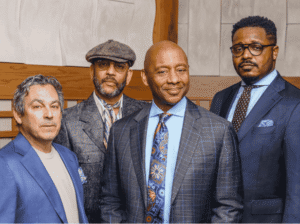 A group portrait of the four members of the Branford Marsalis Quartet, wearing professional suits and stylish attire, including a blazer and a flat cap.