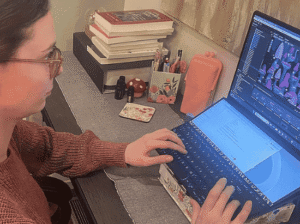 Brittany Westlund, a graduate student from Kalispell, sits at a desk working on a colorful video game project using a dual-screen laptop.
