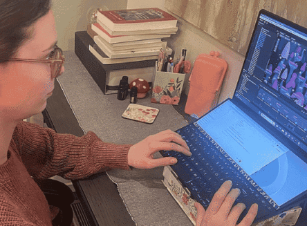 Brittany Westlund, a graduate student from Kalispell, sits at a desk working on a colorful video game project using a dual-screen laptop.