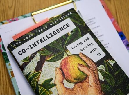 A close-up of the book Co-Intelligence: Living and Working with AI by Ethan Mollick resting on a clipboard.