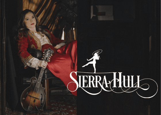 A promotional graphic for bluegrass artist Sierra Hull, featuring her seated in a red dress with her mandolin, set against an artistic, dark-toned background with the "Sierra Hull" logo.